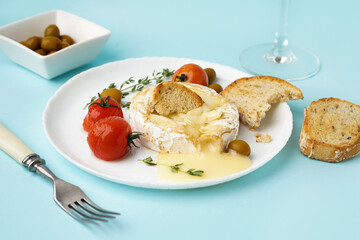 Plate of tasty baked Camembert cheese on blue background