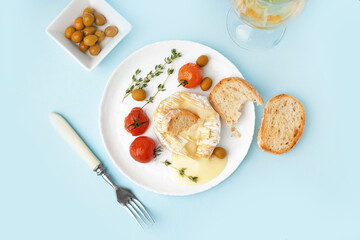 Plate of tasty baked Camembert cheese on blue background