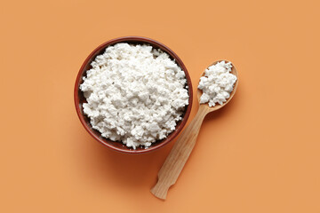 Bowl and spoon of tasty cottage cheese on orange background