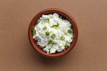Bowl of tasty cottage cheese on brown background