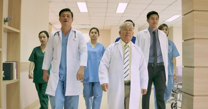 Dolly shot of A group of Asian male and female medical practitioners and senior doctor walking together in hospital hallway. Confident medical team ready to treating patients. healthcare concept.