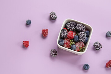 Bowl of frozen berries on purple background