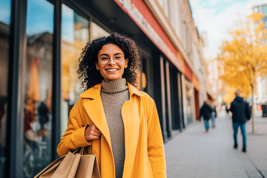 happy african american woman in yellow coat with shopping bags in city. selective focus.