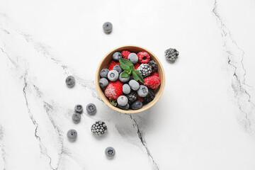 Bowl of frozen berries with mint leaves on white grunge background