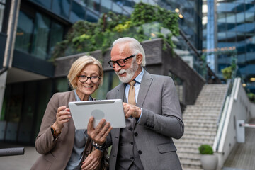 Obraz premium senior man dressed in a suit and a mature blonde woman as business partners husband and wife friends or colleagues talk With digital tablet in hand browse internet look data exchange ideas copy space