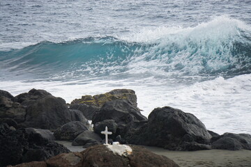 waves crashing on rocks on the tropical island of La Réunion, France with a white cross on shore