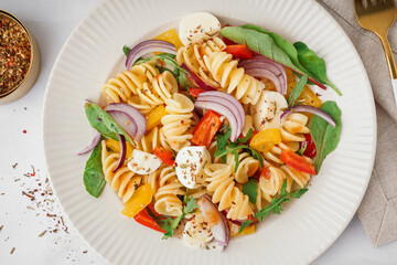 Plate of tasty pasta salad with pepper and red onion on white background