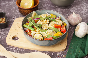 Bowl of tasty pasta salad with pepper and red onion on dark background