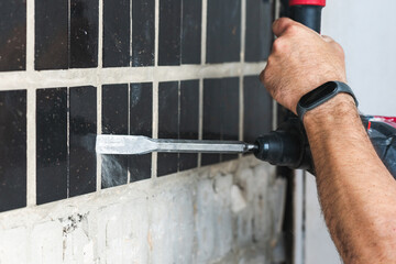 Builder with a puncher dismantles old tiles from a concrete wall