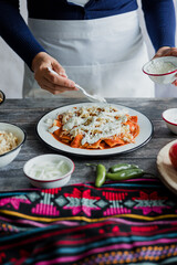 Mexican woman hands preparing chilaquiles with red sauce and eating traditional mexican food for breakfast in Mexico Latin America