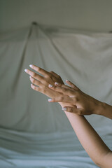 close up of woman hands and arms crossed on bed sheet with delicate soft natural light. Concept of hand care and manicure. white nails.