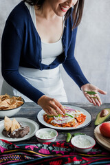 Mexican woman preparing chilaquiles with red sauce and eating traditional mexican food for breakfast in Mexico Latin America, hispanic people
