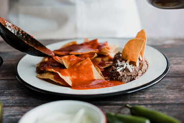 Mexican woman hands preparing chilaquiles with red sauce and eating traditional mexican food for breakfast in Mexico Latin America
