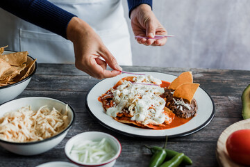 Mexican woman hands preparing chilaquiles with red sauce and eating traditional mexican food for breakfast in Mexico Latin America