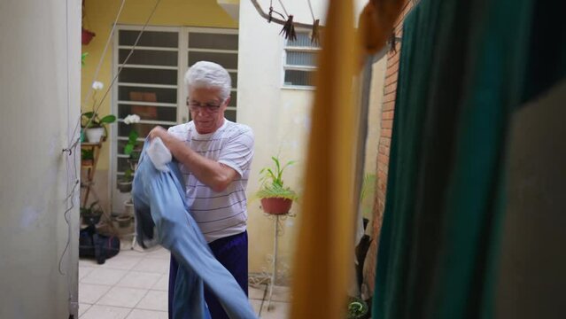 Senior man reverting pants from the inside out after drying on hanger, older person doing domestic chore routine by straightening jeans