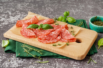 Wooden board with slices of tasty salami on grey background