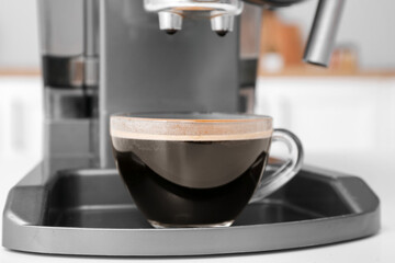 Modern coffee machine with glass cup of hot espresso on white table, closeup