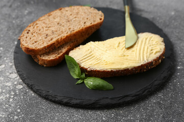 Fototapeta na wymiar Board of tasty toast with butter and basil on grey background