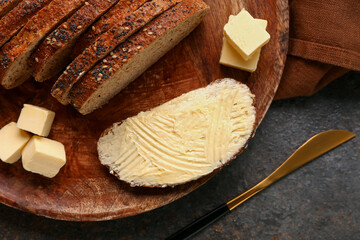Wooden board with tasty toast with butter on dark background, closeup