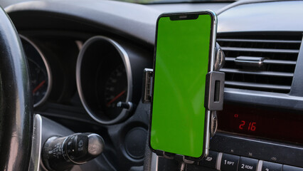 Smartphone or GPS, navigator device in a holder in car with blur background of traffic jams in the evening. Mockup green empty screen for text, copy space
