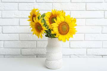 Vase with sunflowers on table near white brick wall