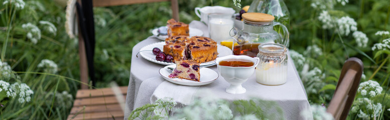 Elegant glamour table setting outdoor in the garden. White porcelain cups, teapot with herbal tea, homemade cherry sweet pie. Family tradition, beautiful place outside. Flower meadow, candles. Banner