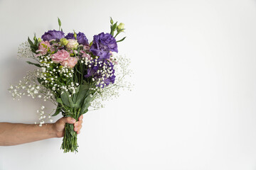 Mans hand holds bouquet of beautiful violet and pink flowers on white background.