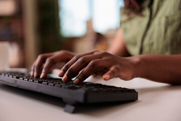 Closeup of african american influencer writing post for social media on computer keyboard while working remote from home living room. Selective focus on woman hands typing blog article.