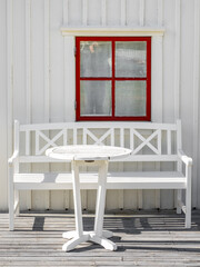 Fototapeta na wymiar A white wooden Swedish house with a red window, and a white bench and table on the veranda on the island of Vrango, Sweden