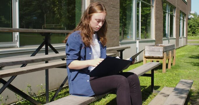 Frustrated student sitting on bleachers while studying in front of a school