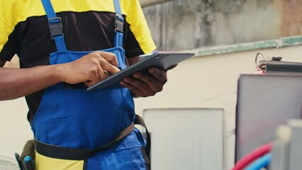 Close up of skillful technician commissioned for outside hvac system routine maintenance, looking for refrigerant issues. Meticulous mechanic doing air conditioner inspection, writing data on tablet
