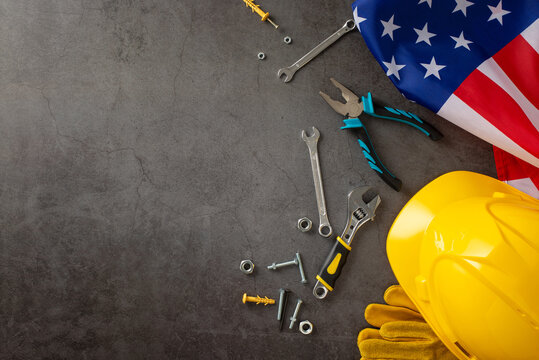 Honoring the hard work of construction workers on Labor Day. Top-down image showcasing flag, helmet, gloves, and building tools on grunge textured grey concrete. Suitable for ads or text