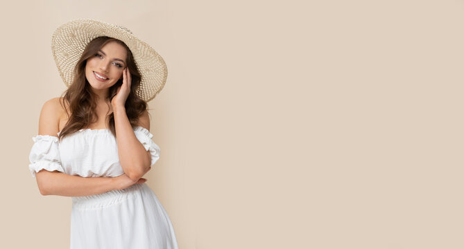 Very attractive brunette in straw hat and white dress on creamy background.