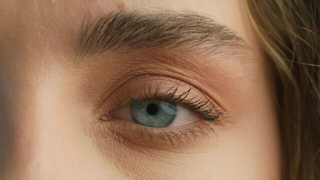 Close up of womans Face. Young attractive girl opening her Beautiful blue azzure eyes. Natural Beauty with thick eyebrows. Gorgeous woman with long Eyelashes and Attractive face. Slow motion beauty 4K
