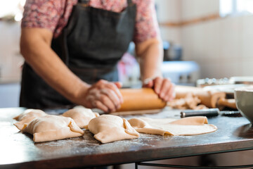 Unrecognizable Latin Woman Kneading Dough with a Rolling Pin, for making Empanadas in her Countryside Home Kitchen