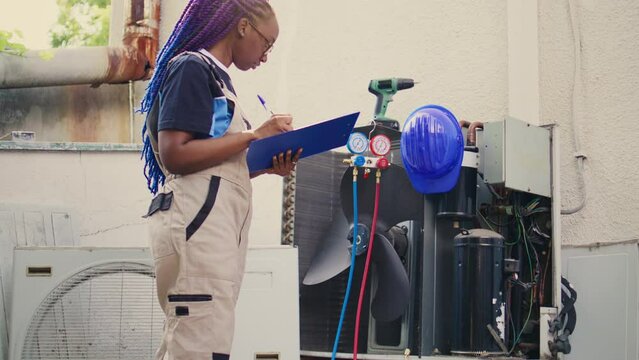 Revealing portrait shot of worker doing inspection of freon levels and necessary repairs to prevent major breakdowns. Capable electrician troubleshooting hvac system, writing findings on clipboard