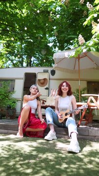 slow motion of Two beautiful hippie girls are singing a song sitting on the terrace near the trailer with a guitar.