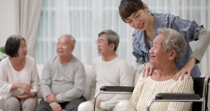 A beautiful kindness young Asian nurse stand behind the old woman in wheelchair and massage her shoulders and they talking with a smile at nursing home. the other senior chatting together on the back.