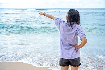 Rear view of an Asian woman pointing at something while traveling on the beach