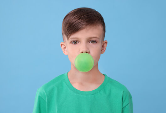 Boy blowing bubble gum on light blue background