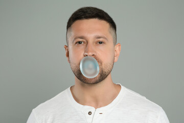 Handsome man blowing bubble gum on light grey background