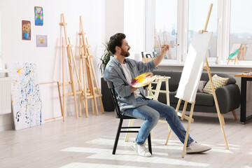 Man painting in studio. Using easel to hold canvas