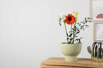 Stylish ikebana as house decor. Beautiful fresh flowers on wooden table near white wall, space for text