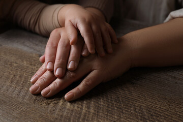Family holding hands together at wooden table, closeup
