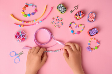 Child making beaded jewelry and different supplies on pink background, top view. Handmade accessories