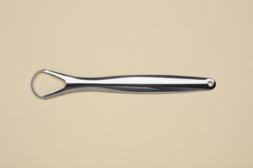Metal tongue cleaner on beige background, top view
