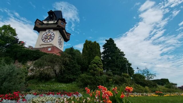 Cityscape of old town of Graz and the Clock Tower (Grazer Uhrturm), famous tourist attraction in Steiermark, Austria, in cloudy summer day in 4k