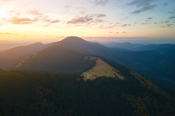Obraz premium Aerial view of bright foggy morning over dark peak with mountain forest trees at autumn sunrise. Beautiful scenery of wild woodland at dawn