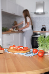 Pregnant young woman preparing healthy sandwiches with microgreens and vegetables at home in the kitchen