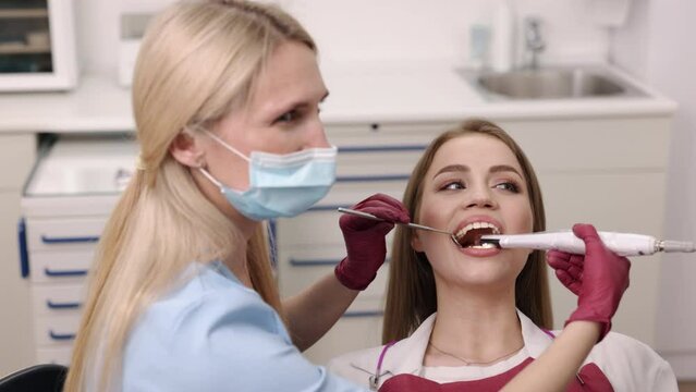 Dental technology, dental imaging, patient checkup. Intraoral camera assists dentist in examining oral cavity of young woman meticulously.